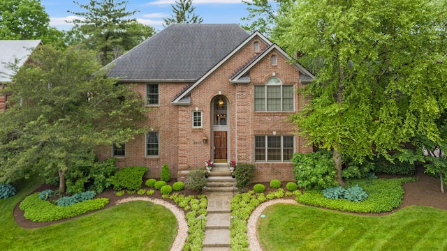 view of front of house with brick siding, a front yard, and a shingled roof