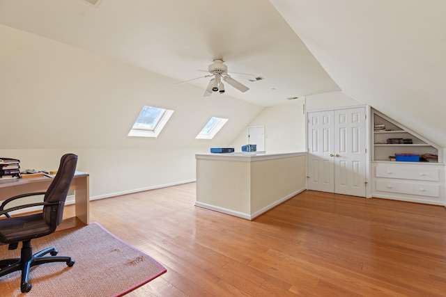 office area with a skylight, vaulted ceiling, light wood-style floors, ceiling fan, and baseboards