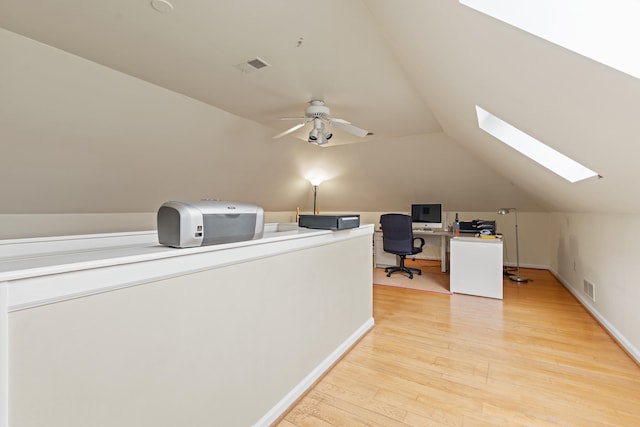 office area with a skylight, vaulted ceiling, light wood-type flooring, ceiling fan, and baseboards