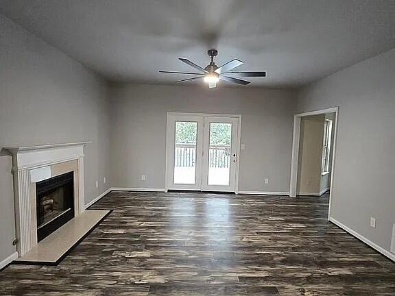 unfurnished living room featuring baseboards, a fireplace, wood finished floors, and a ceiling fan
