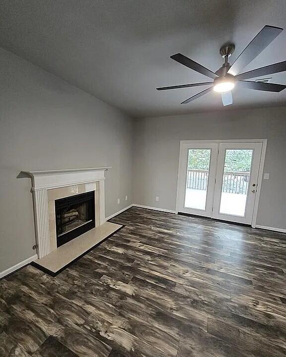 unfurnished living room featuring baseboards, a fireplace, ceiling fan, and dark wood-style flooring