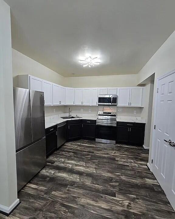 kitchen with light countertops, white cabinets, stainless steel appliances, a sink, and dark cabinets