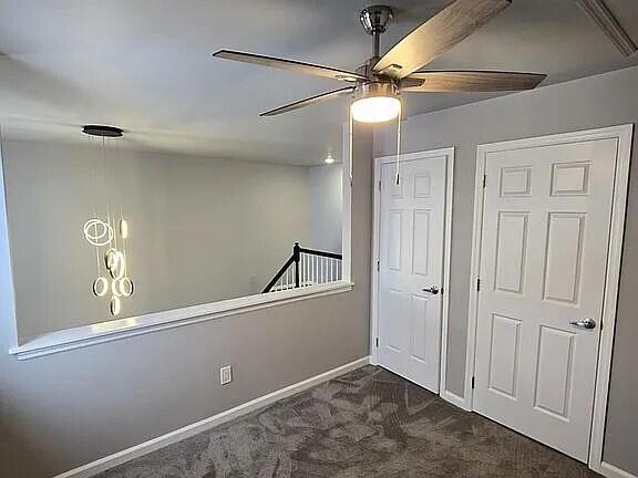 interior space with baseboards, dark carpet, and a ceiling fan