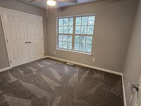 unfurnished bedroom with a closet, visible vents, baseboards, a ceiling fan, and dark carpet