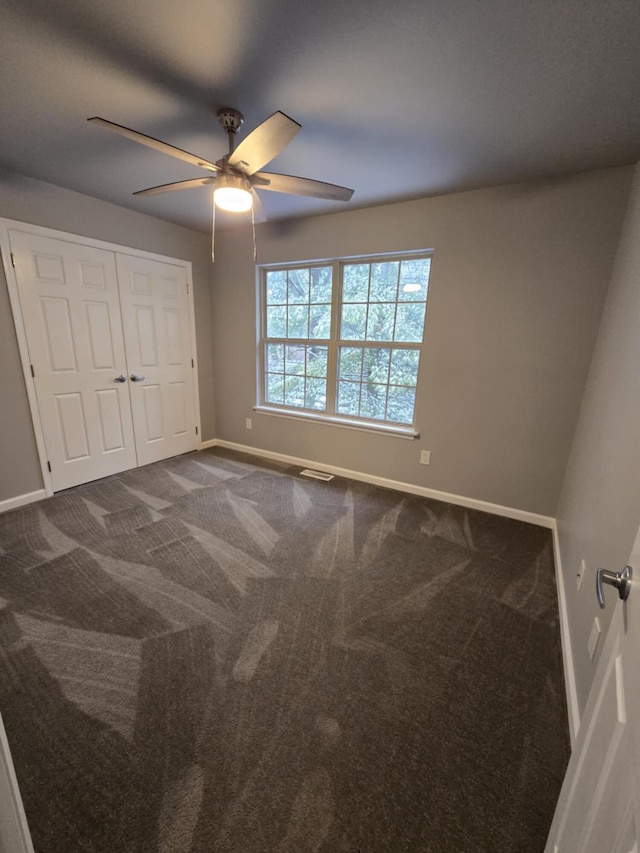 unfurnished bedroom with a closet, baseboards, ceiling fan, and dark carpet