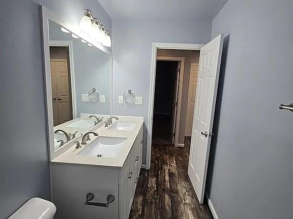 bathroom with toilet, a sink, double vanity, and wood finished floors