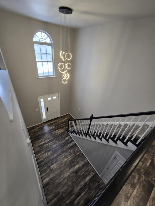 foyer entrance featuring a towering ceiling, wood finished floors, and an inviting chandelier