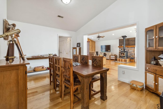dining area with visible vents, a ceiling fan, lofted ceiling, light wood-style floors, and a wood stove