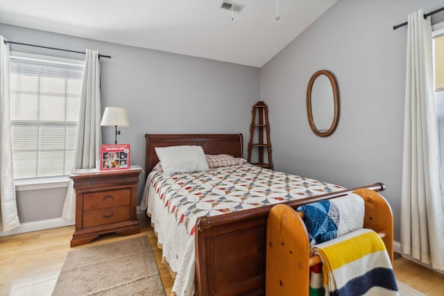 bedroom featuring wood finished floors, baseboards, lofted ceiling, and visible vents
