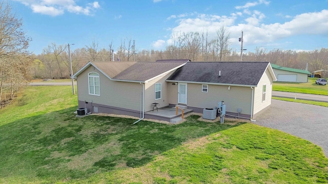 rear view of property with driveway, a shingled roof, central AC, and a yard