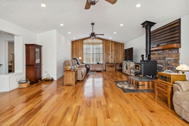 living room featuring vaulted ceiling, light wood finished floors, a wood stove, baseboards, and ceiling fan