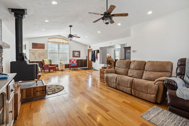 living room featuring vaulted ceiling, a ceiling fan, a wood stove, light wood-style flooring, and recessed lighting