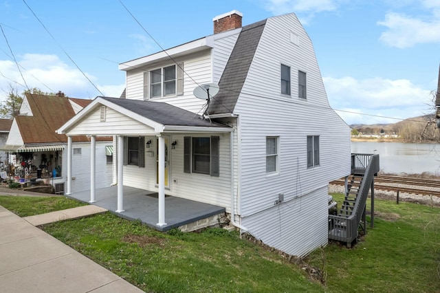 view of front of house with a front lawn, a chimney, a shingled roof, a porch, and a water view