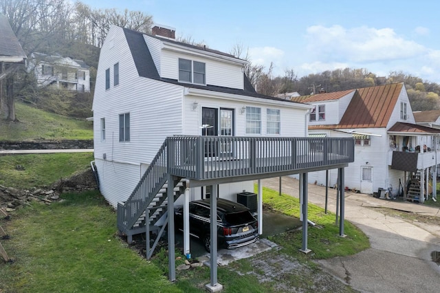 rear view of property featuring a deck, stairs, a lawn, driveway, and a carport