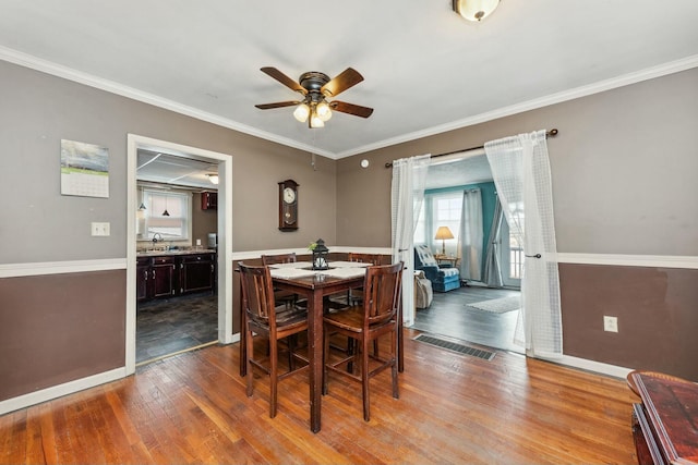 dining area featuring baseboards, ornamental molding, a ceiling fan, and wood finished floors