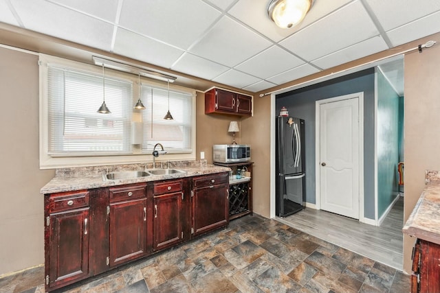 kitchen featuring dark brown cabinets, a sink, a paneled ceiling, freestanding refrigerator, and stainless steel microwave