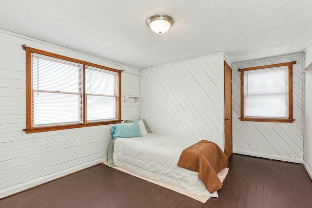 bedroom with baseboards, wood walls, dark wood-style floors, and a textured ceiling