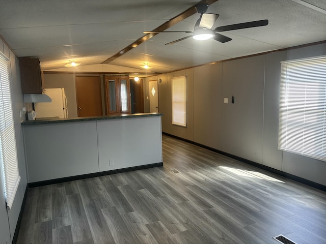 interior space featuring a ceiling fan, a peninsula, lofted ceiling, dark countertops, and dark wood-style flooring