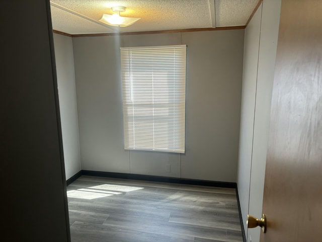 unfurnished room with a textured ceiling, baseboards, and wood finished floors