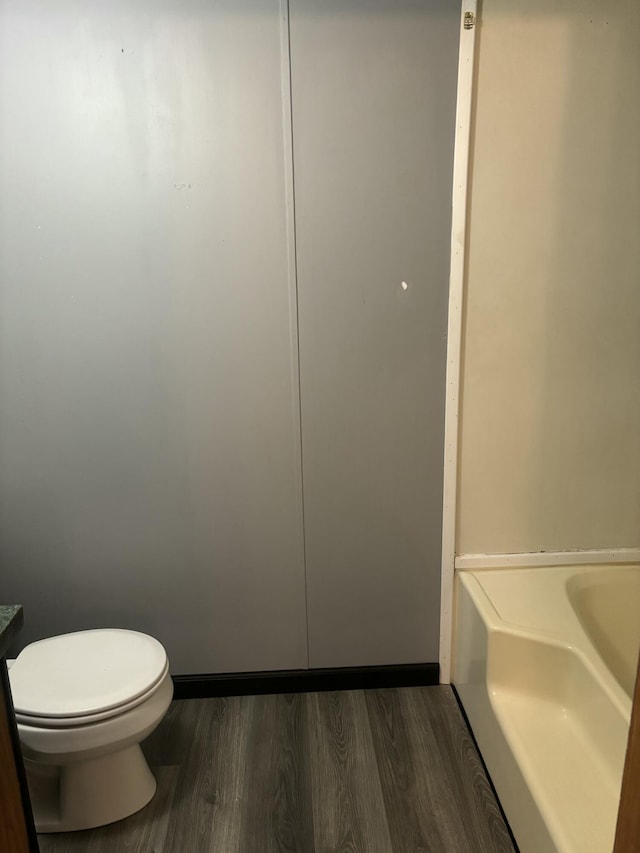 full bathroom with baseboards, wood finished floors, toilet, and a bathtub