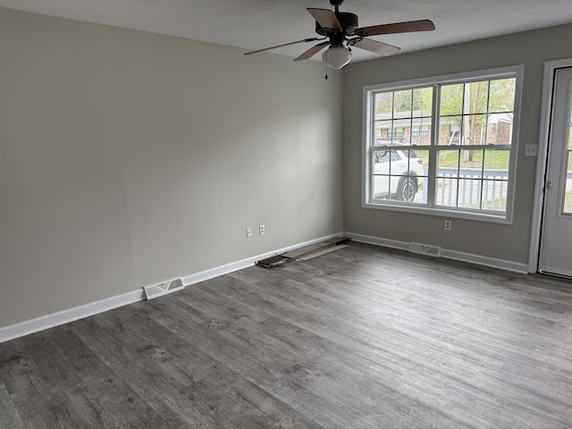 spare room featuring baseboards, visible vents, a ceiling fan, and dark wood finished floors
