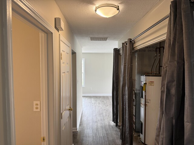 hallway featuring a textured ceiling, visible vents, baseboards, dark wood-style floors, and electric water heater