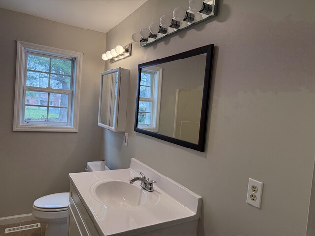 half bathroom featuring a wealth of natural light, visible vents, toilet, and vanity