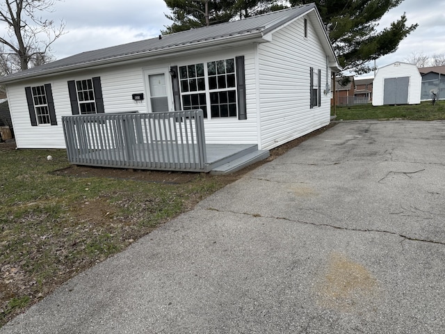 view of front of property with an outdoor structure, metal roof, a storage unit, aphalt driveway, and a deck