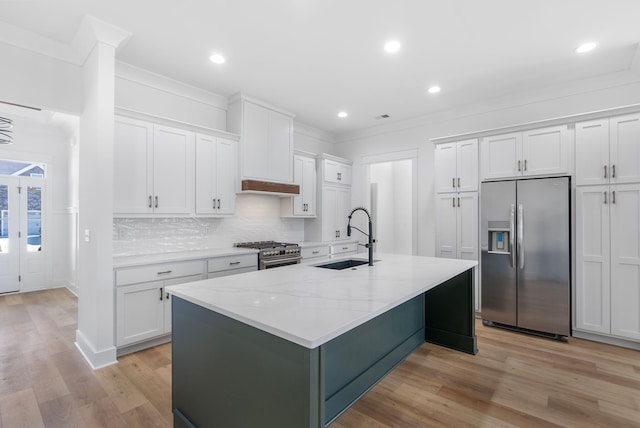 kitchen featuring white cabinets, a kitchen island with sink, a sink, stainless steel appliances, and decorative backsplash