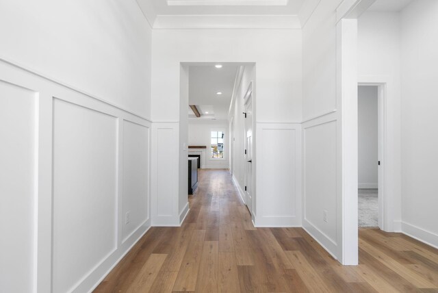 hallway featuring a decorative wall, wood finished floors, ornamental molding, and a wainscoted wall