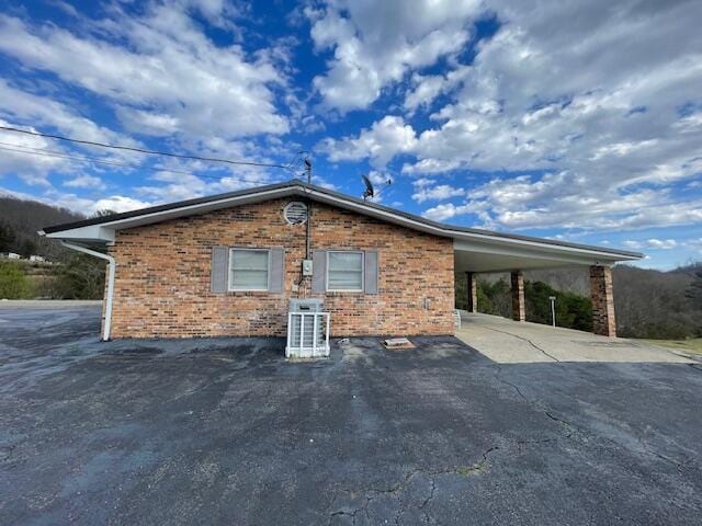 view of side of home featuring an attached carport, cooling unit, brick siding, and driveway