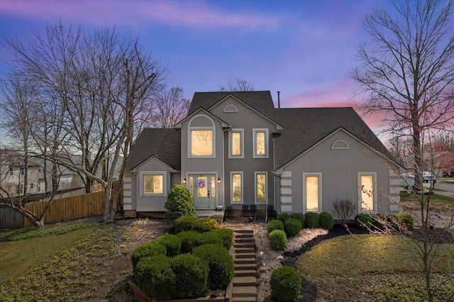 view of front facade featuring fence, a shingled roof, and stucco siding