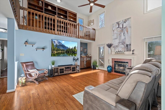 living room with ceiling fan, wood finished floors, a fireplace, and a towering ceiling