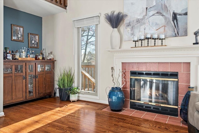 interior space featuring a tile fireplace, baseboards, a dry bar, and wood finished floors