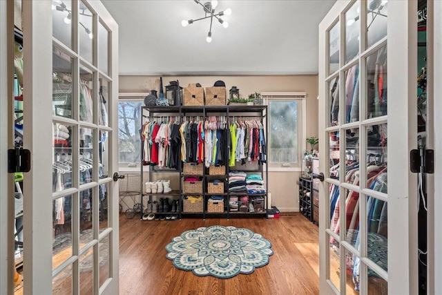 walk in closet with french doors, a notable chandelier, and wood finished floors