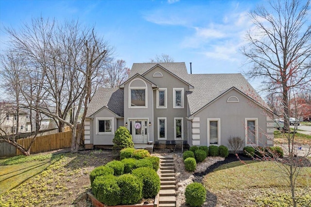 traditional home with fence, a shingled roof, and stucco siding