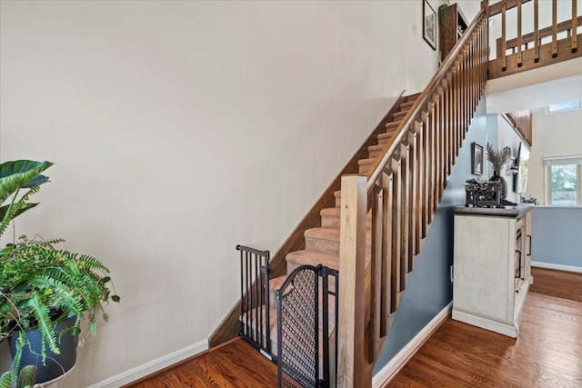 stairs featuring baseboards, a towering ceiling, and wood finished floors