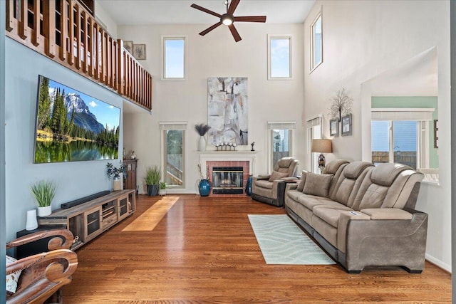 living room featuring a glass covered fireplace, a high ceiling, wood finished floors, and ceiling fan