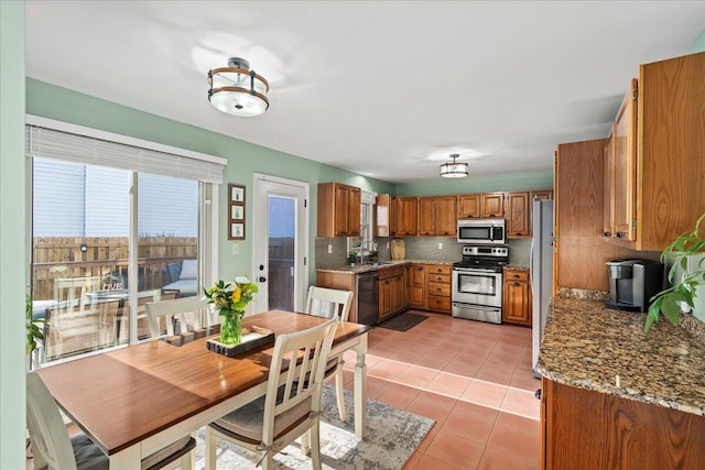 kitchen featuring light tile patterned floors, appliances with stainless steel finishes, a sink, brown cabinets, and backsplash