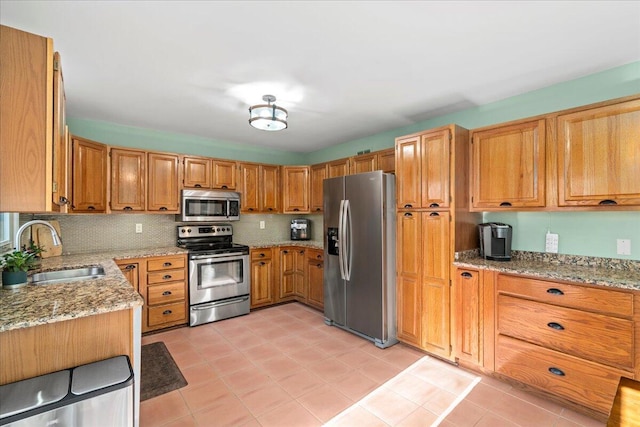 kitchen with light tile patterned floors, light stone countertops, a sink, stainless steel appliances, and backsplash