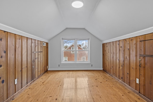 bonus room with lofted ceiling, wood walls, and light wood-type flooring