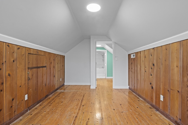 bonus room with baseboards, lofted ceiling, wood walls, and wood-type flooring