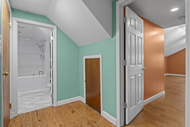 corridor featuring baseboards, vaulted ceiling, and wood finished floors