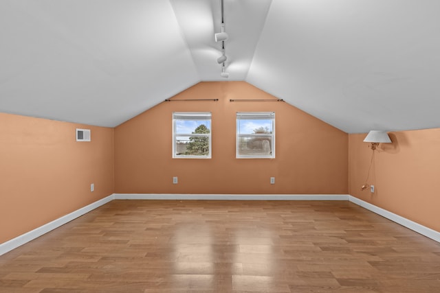 additional living space with light wood-style flooring, baseboards, lofted ceiling, and visible vents