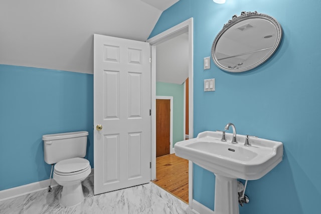 bathroom with lofted ceiling, toilet, baseboards, marble finish floor, and a sink