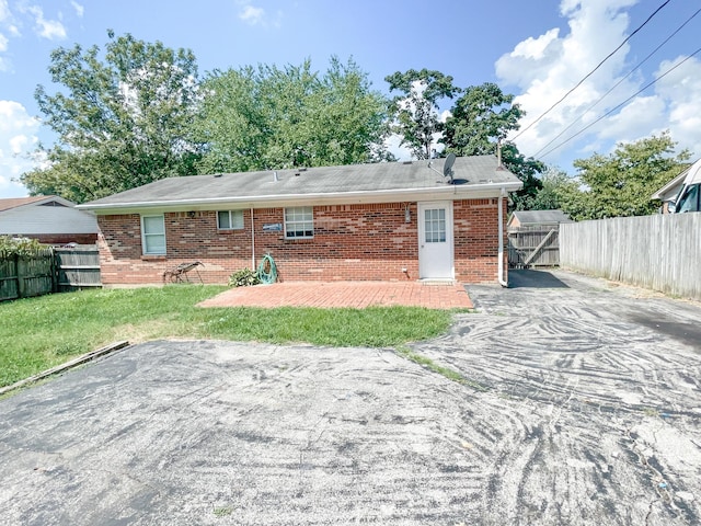 rear view of property featuring brick siding, a patio, fence, and a lawn