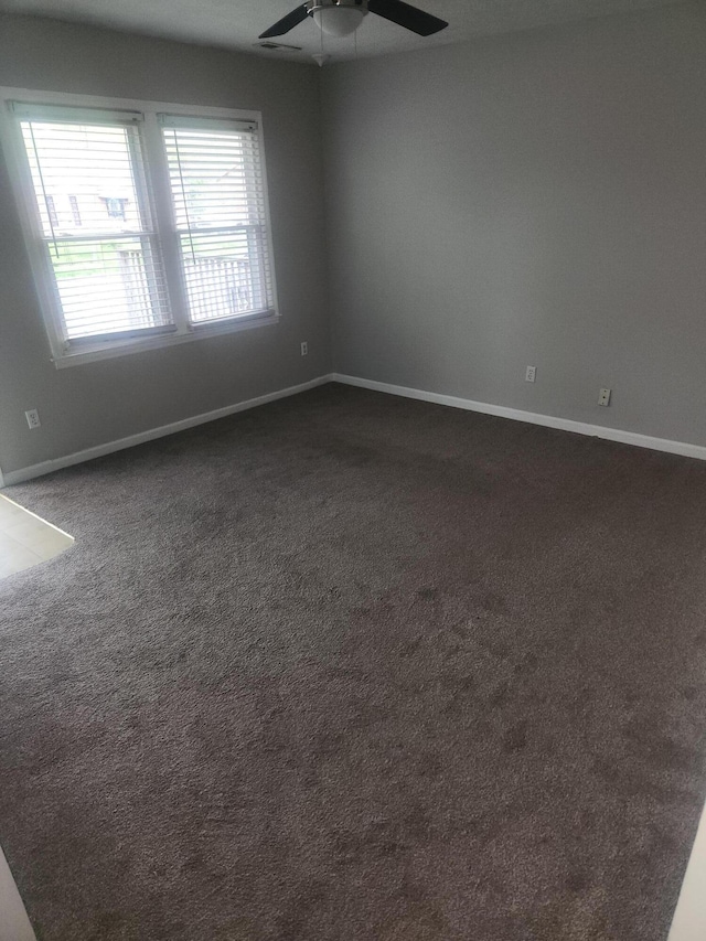 spare room with baseboards, dark colored carpet, and a ceiling fan