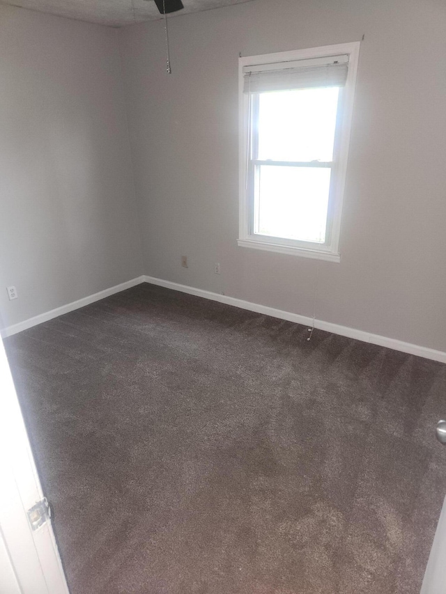 unfurnished room with baseboards and dark colored carpet