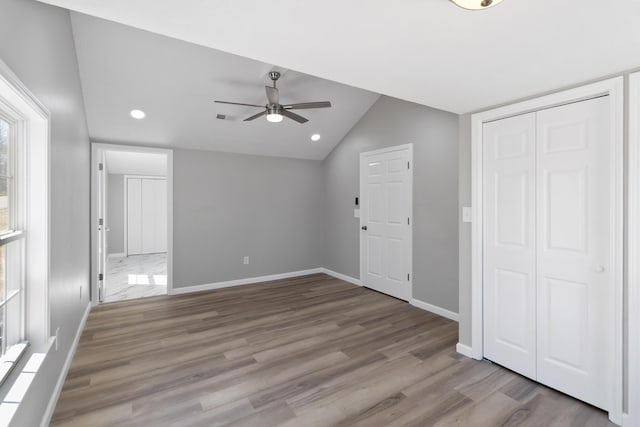 unfurnished bedroom with visible vents, baseboards, a closet, wood finished floors, and lofted ceiling