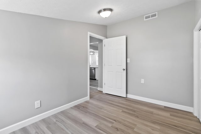 empty room featuring light wood-style flooring, a textured ceiling, baseboards, and visible vents